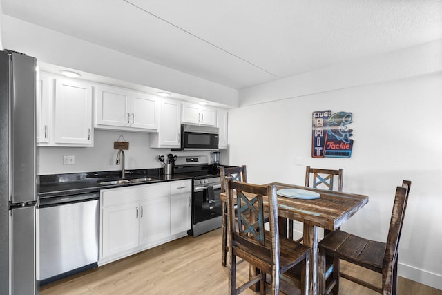 kitchen featuring light wood finished floors, dark countertops, appliances with stainless steel finishes, white cabinets, and a sink