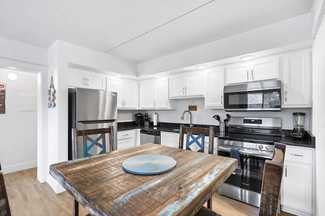 kitchen with dark countertops, light wood finished floors, stainless steel appliances, white cabinetry, and a sink