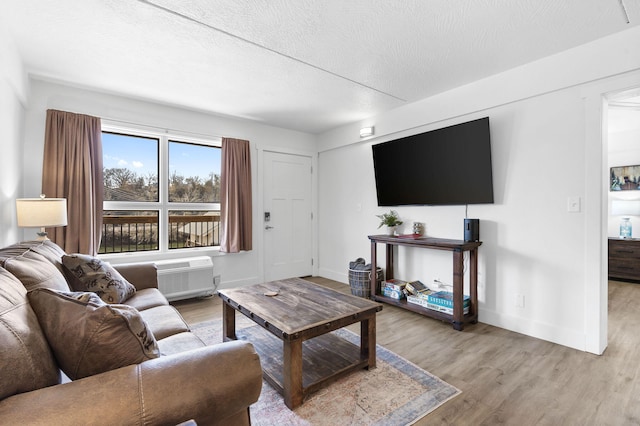 living room featuring light wood-style flooring, baseboards, a wall mounted air conditioner, and a textured ceiling