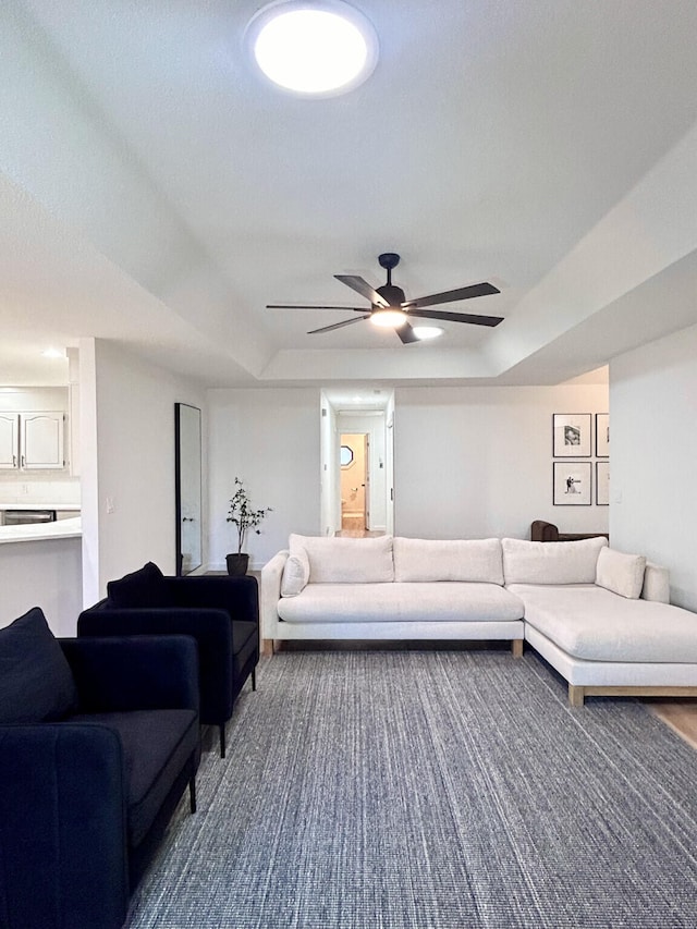 living room featuring a tray ceiling, dark colored carpet, and ceiling fan