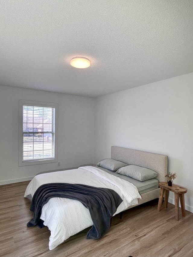 bedroom with baseboards, a textured ceiling, and wood finished floors