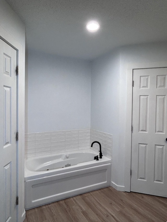 bathroom featuring a garden tub, wood finished floors, and a textured ceiling