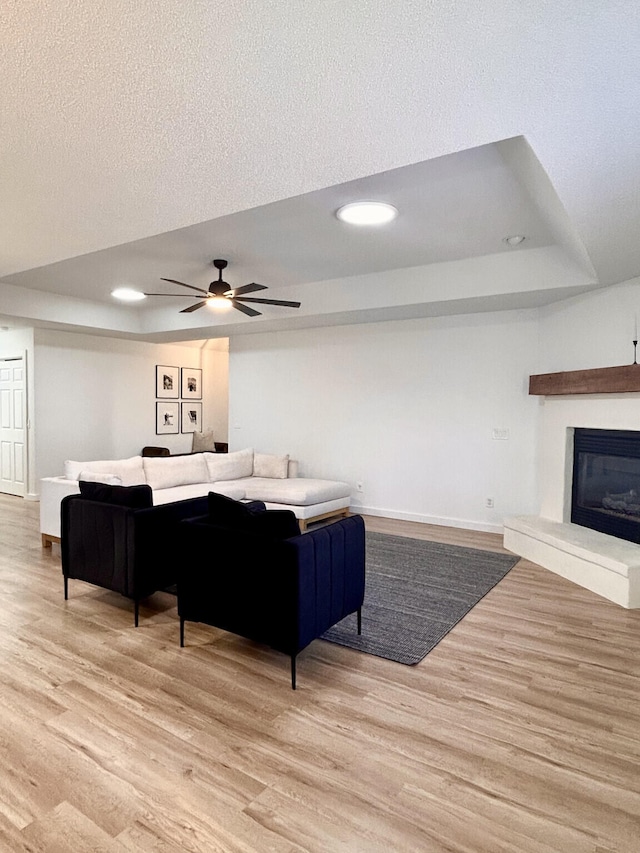 living area with a glass covered fireplace, a tray ceiling, wood finished floors, and baseboards