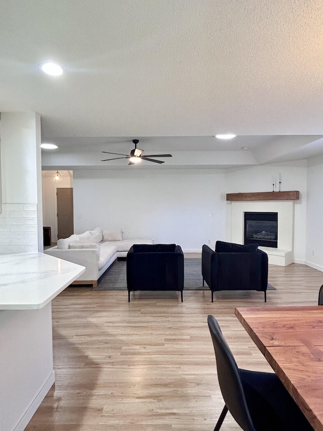 living room with a glass covered fireplace, a textured ceiling, light wood-type flooring, and a ceiling fan