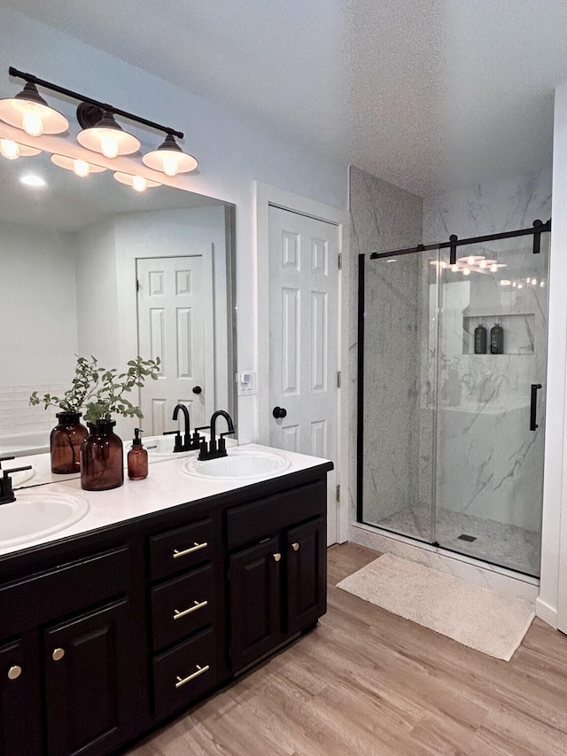 bathroom with a sink, a marble finish shower, wood finished floors, and double vanity