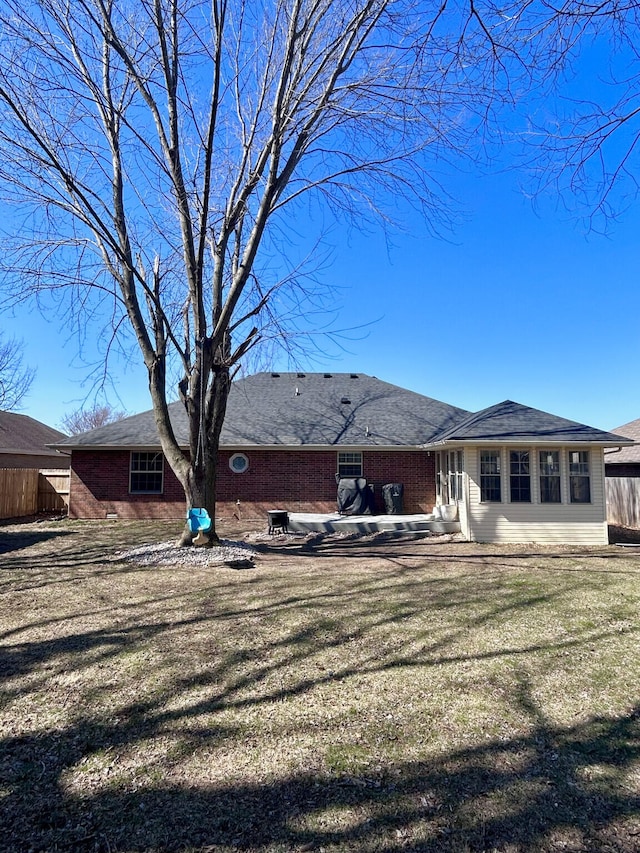 back of house featuring entry steps, a lawn, brick siding, and fence