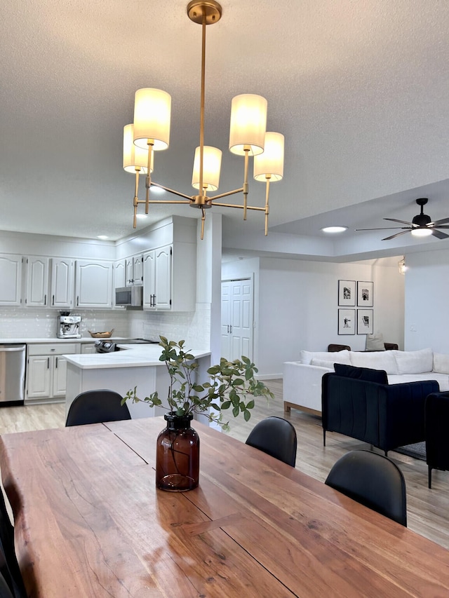 dining area featuring ceiling fan with notable chandelier, light wood-style floors, and a textured ceiling