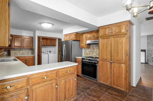 kitchen featuring gas stove, a sink, stainless steel refrigerator with ice dispenser, under cabinet range hood, and washer and dryer