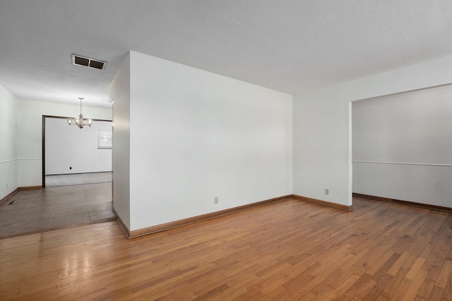 unfurnished room featuring light wood-type flooring, visible vents, baseboards, and a chandelier