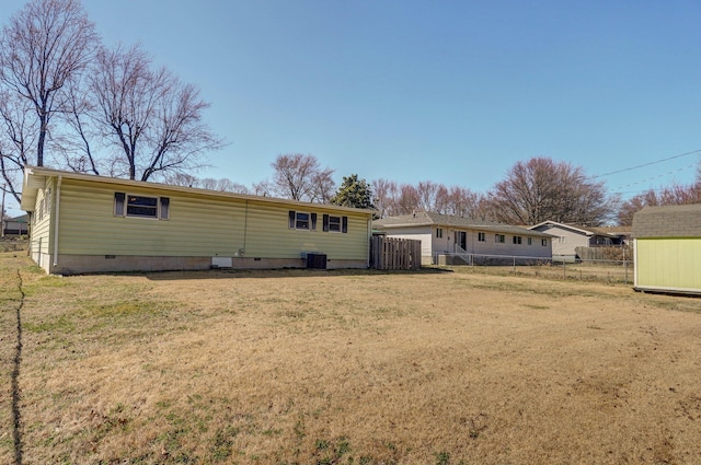 back of property featuring fence, a storage shed, a yard, an outdoor structure, and crawl space