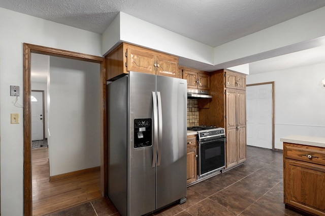 kitchen with stove, stainless steel fridge, brown cabinetry, and under cabinet range hood