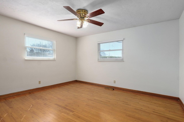 empty room with baseboards, a textured ceiling, a healthy amount of sunlight, and light wood finished floors