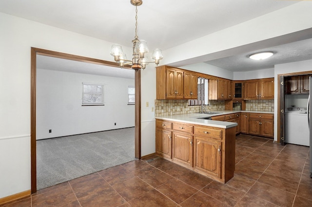 kitchen featuring washer / dryer, brown cabinets, a notable chandelier, and a peninsula