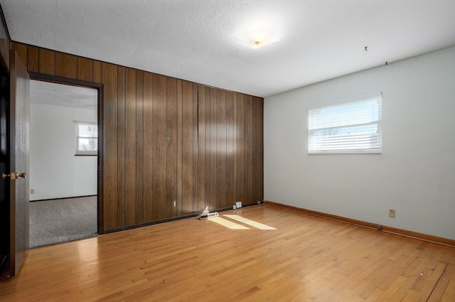 unfurnished room featuring wooden walls, a textured ceiling, light wood-type flooring, and baseboards