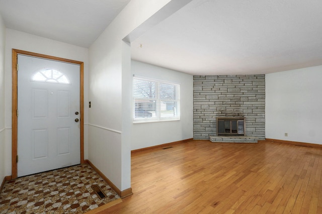 entryway featuring light wood finished floors, a stone fireplace, and baseboards