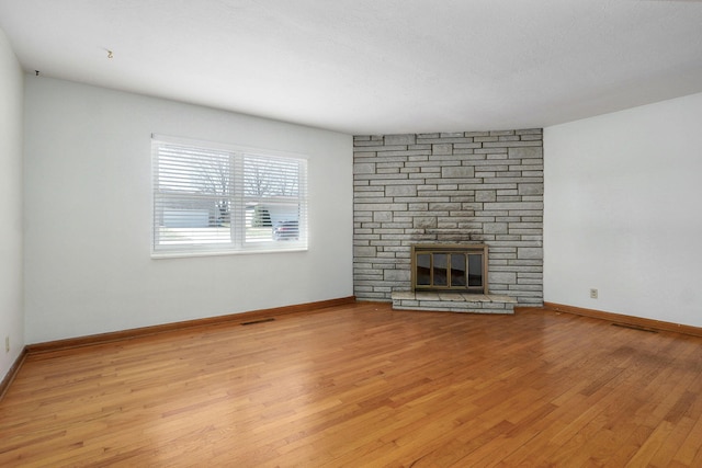 unfurnished living room with a stone fireplace, visible vents, light wood-style floors, and baseboards