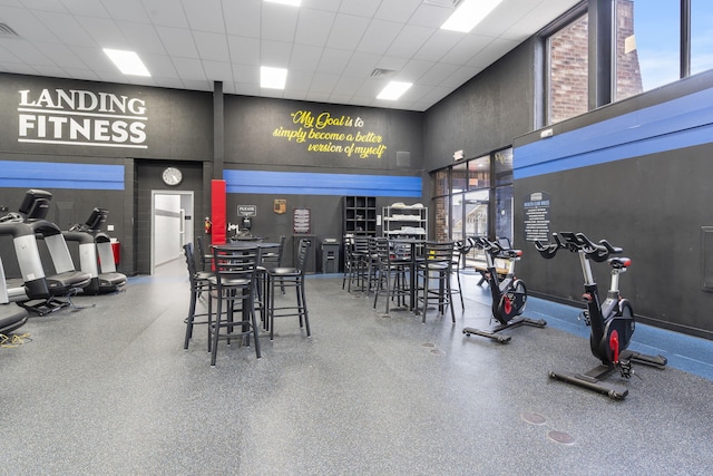 gym featuring a drop ceiling, visible vents, a healthy amount of sunlight, and a towering ceiling