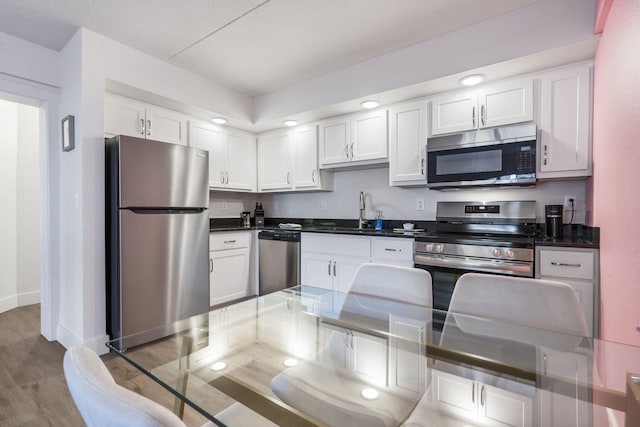 kitchen featuring a sink, dark countertops, wood finished floors, stainless steel appliances, and white cabinets