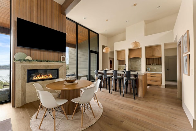 dining room featuring a premium fireplace, light wood-style flooring, a towering ceiling, and expansive windows