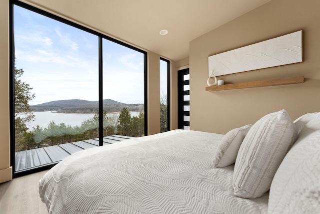 bedroom with a wall of windows, a water view, and wood finished floors