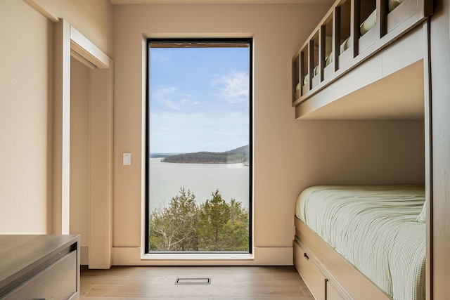 bedroom with multiple windows, light wood-type flooring, and a water view