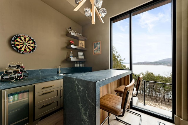 bar with a water view, lofted ceiling, beverage cooler, dark wood finished floors, and wet bar