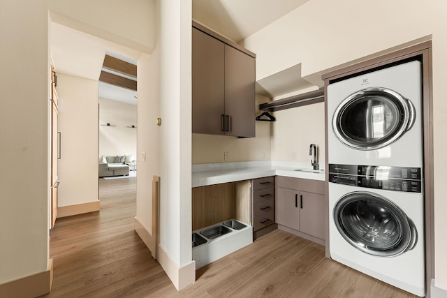 washroom featuring a sink, cabinet space, light wood-style floors, and stacked washing maching and dryer