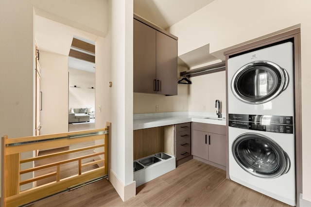 laundry area with light wood finished floors, cabinet space, a sink, and stacked washing maching and dryer