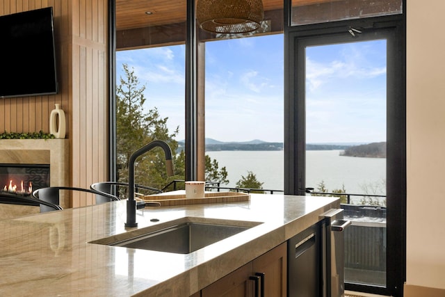 kitchen featuring a sink, a water view, a fireplace, and light stone countertops