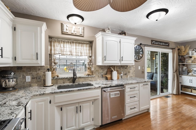 kitchen with backsplash, light wood-style flooring, stainless steel dishwasher, white cabinetry, and a sink