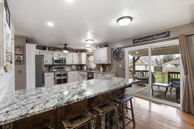 kitchen with light stone countertops, a peninsula, decorative backsplash, light wood-style floors, and appliances with stainless steel finishes