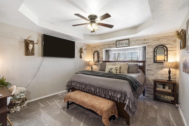 bedroom featuring baseboards, a tray ceiling, carpet flooring, a textured ceiling, and a ceiling fan