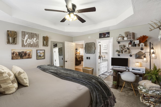 carpeted bedroom with a tray ceiling, a ceiling fan, and ensuite bathroom