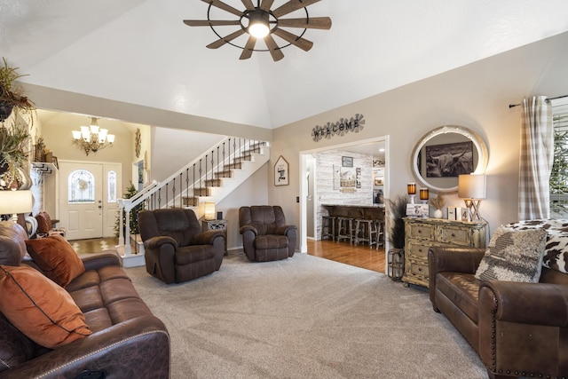 carpeted living area featuring ceiling fan with notable chandelier, high vaulted ceiling, and stairs