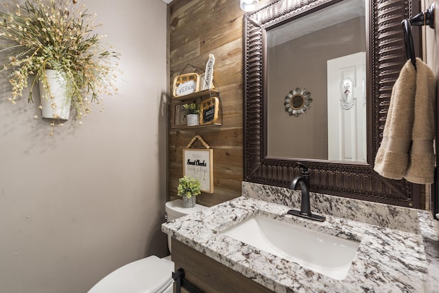 bathroom featuring vanity, toilet, and wooden walls