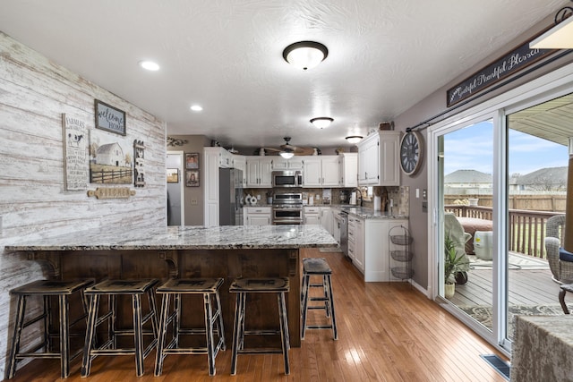 kitchen with a sink, white cabinetry, appliances with stainless steel finishes, a peninsula, and light stone countertops