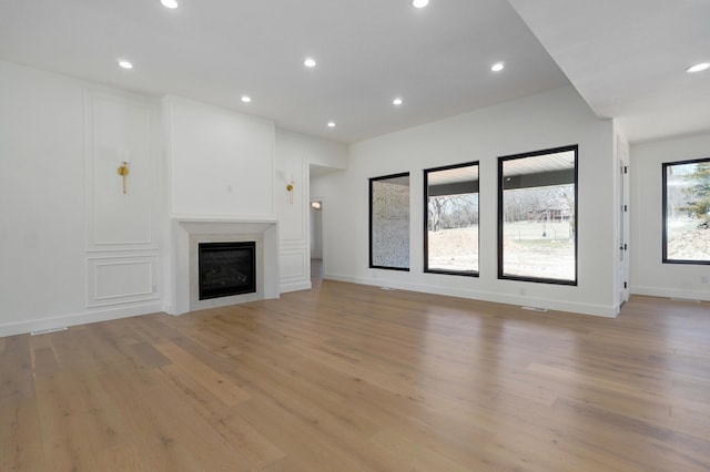 unfurnished living room with a glass covered fireplace, recessed lighting, light wood-style floors, and baseboards