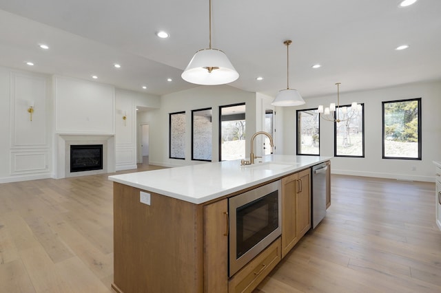 kitchen featuring a sink, stainless steel appliances, open floor plan, a glass covered fireplace, and light wood-type flooring