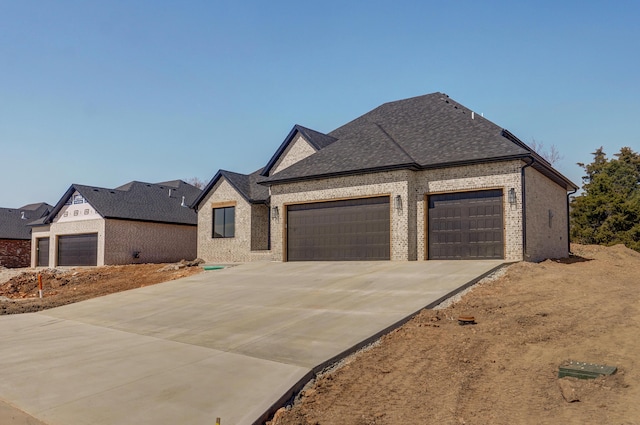 french country style house featuring a garage, brick siding, roof with shingles, and driveway