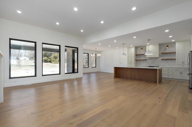 unfurnished living room featuring baseboards, recessed lighting, a sink, light wood-type flooring, and a chandelier