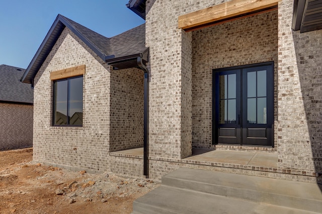 doorway to property with french doors, brick siding, and a shingled roof