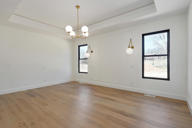 empty room featuring visible vents, baseboards, an inviting chandelier, light wood-style floors, and a raised ceiling