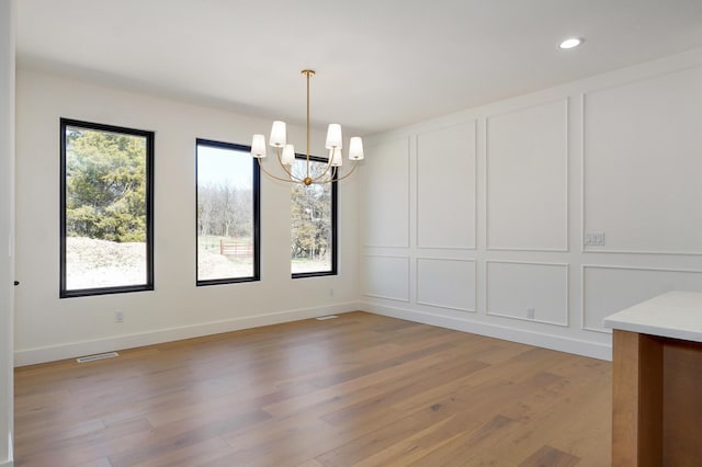 unfurnished dining area with a notable chandelier, a decorative wall, plenty of natural light, and light wood-style floors