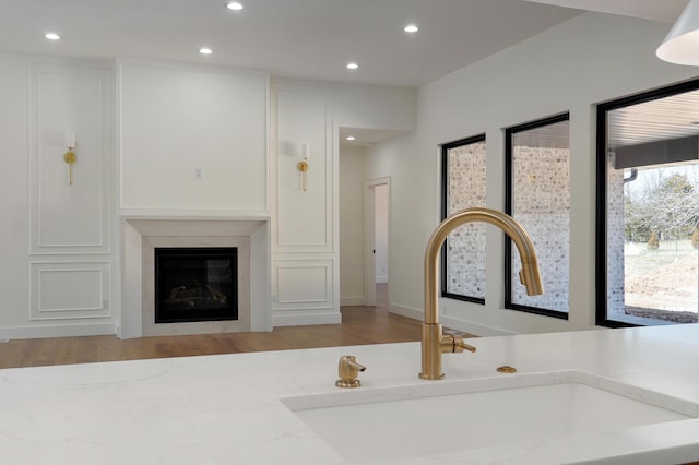 interior space with a glass covered fireplace, recessed lighting, wood finished floors, and a sink