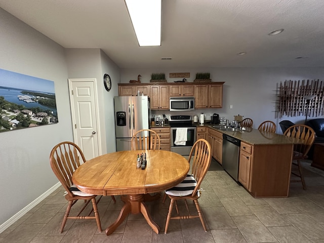 kitchen featuring baseboards, a peninsula, stainless steel appliances, a kitchen bar, and dark countertops