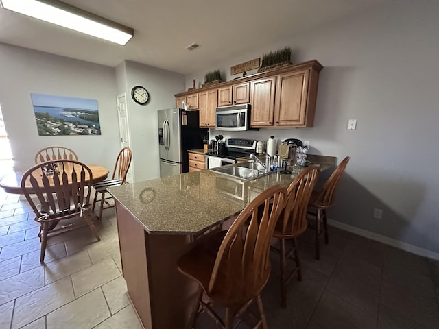 kitchen featuring visible vents, a peninsula, a sink, appliances with stainless steel finishes, and a kitchen breakfast bar