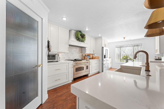 kitchen featuring premium range hood, a sink, double oven range, decorative backsplash, and dark wood-style flooring