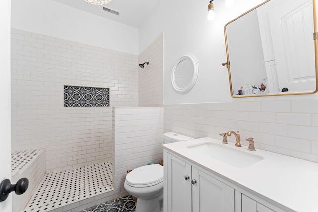 bathroom with visible vents, tile walls, toilet, tiled shower, and vanity