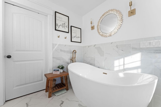 full bath featuring tile walls, a soaking tub, marble finish floor, and wainscoting