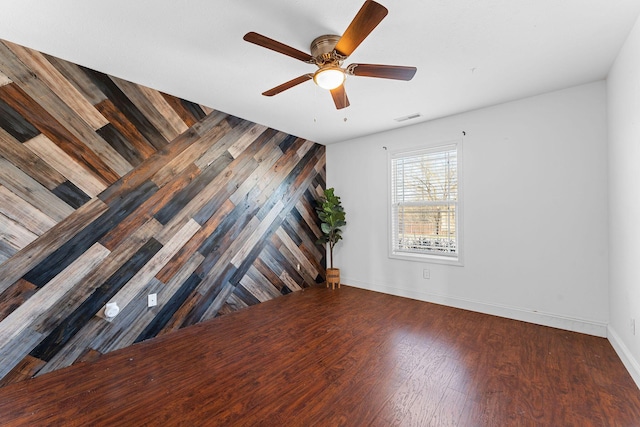 unfurnished room with wooden walls, wood finished floors, visible vents, baseboards, and ceiling fan